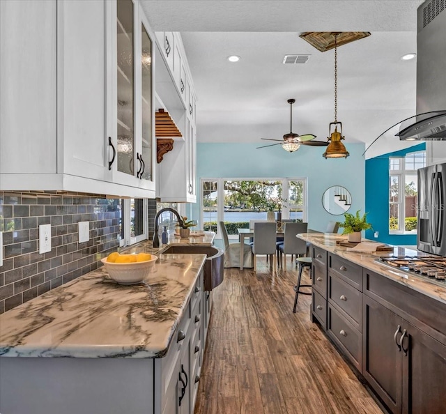 kitchen featuring a healthy amount of sunlight, exhaust hood, appliances with stainless steel finishes, white cabinetry, and hardwood / wood-style flooring