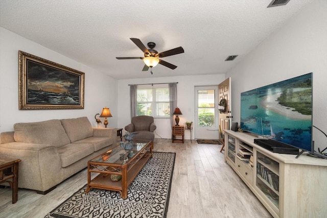 living room with ceiling fan, light wood-type flooring, and a textured ceiling