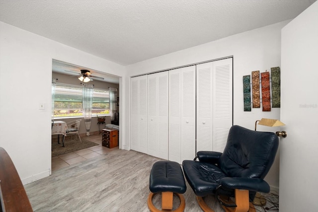 living area with a textured ceiling, ceiling fan, and light hardwood / wood-style floors