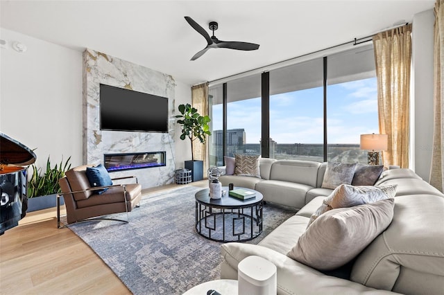 living room featuring floor to ceiling windows, light hardwood / wood-style flooring, ceiling fan, and a premium fireplace