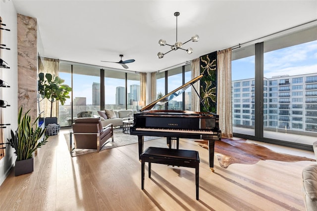 misc room with light hardwood / wood-style flooring, ceiling fan with notable chandelier, and expansive windows