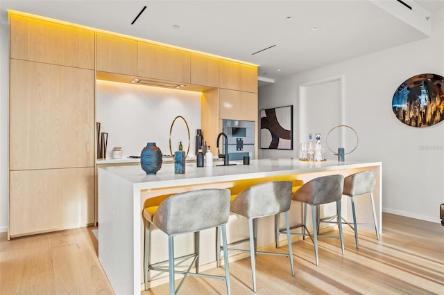 kitchen with a kitchen bar, light hardwood / wood-style floors, a kitchen island with sink, and light brown cabinetry