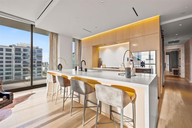 kitchen with a kitchen breakfast bar, an island with sink, floor to ceiling windows, and light wood-type flooring