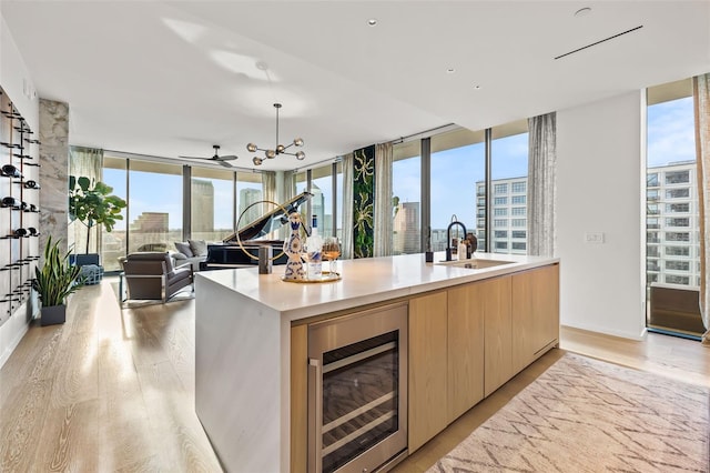 kitchen featuring beverage cooler, sink, light hardwood / wood-style floors, and a center island with sink