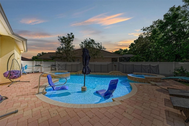 pool at dusk with a patio area and an in ground hot tub