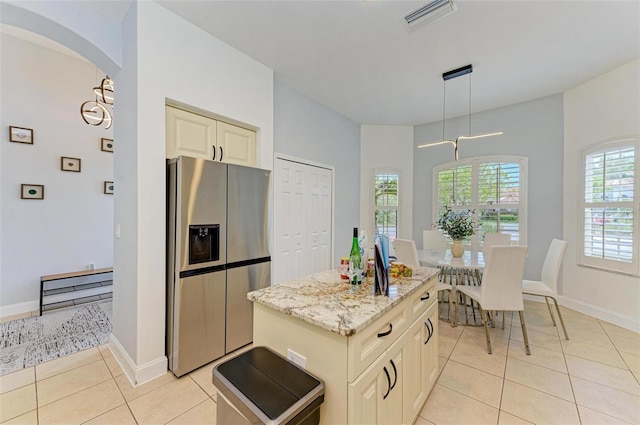 kitchen with pendant lighting, light tile flooring, light stone countertops, a kitchen island, and stainless steel fridge