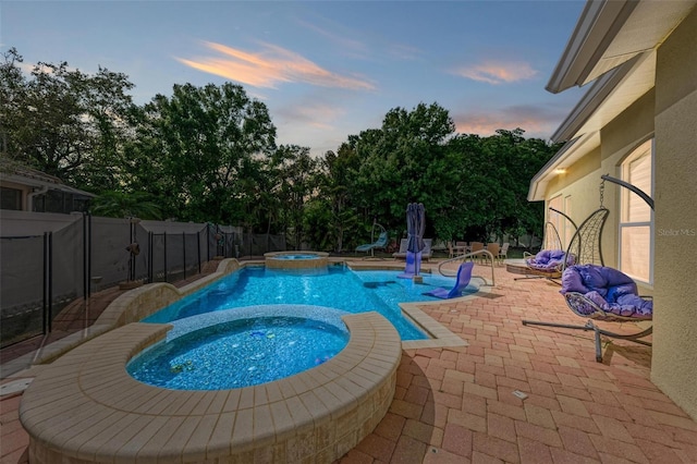 pool at dusk with a patio area and an in ground hot tub