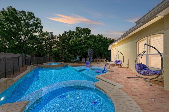 pool at dusk featuring an in ground hot tub and a patio area