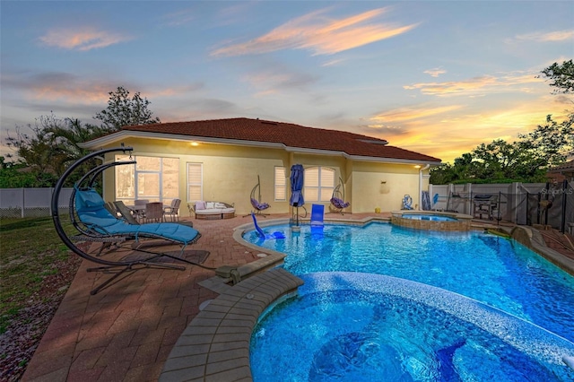 pool at dusk with a patio area and an in ground hot tub