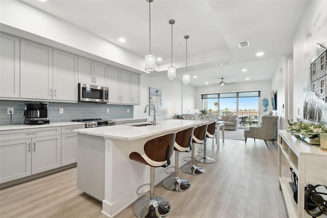 kitchen with visible vents, a sink, tasteful backsplash, light wood-style floors, and appliances with stainless steel finishes