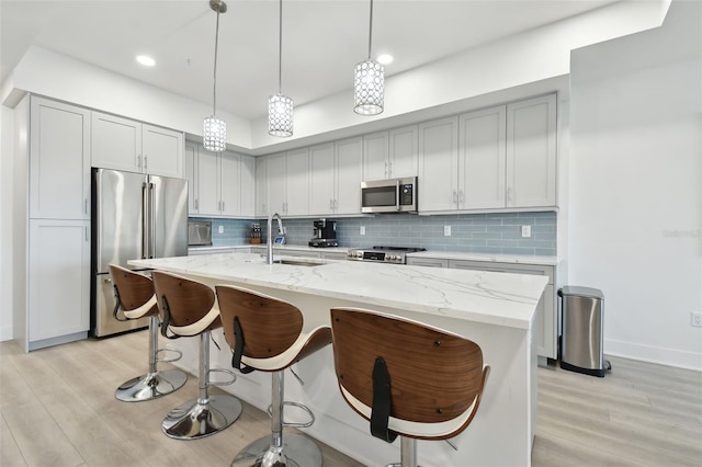 kitchen with a sink, light stone counters, light wood-style floors, and appliances with stainless steel finishes