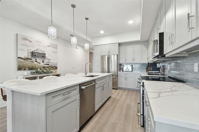 kitchen featuring an island with sink, a sink, backsplash, stainless steel appliances, and light wood-style floors