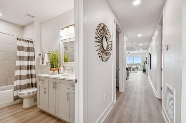 hallway with light wood finished floors, visible vents, recessed lighting, and a sink