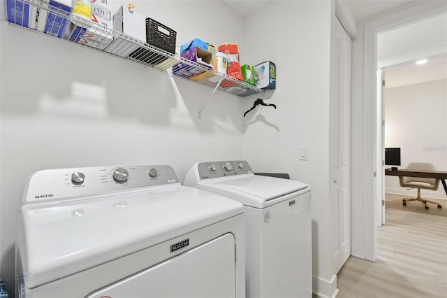 clothes washing area with light wood-style floors, baseboards, separate washer and dryer, and laundry area