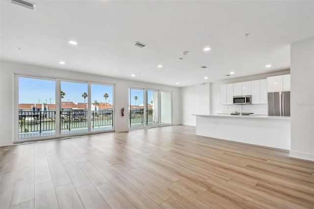 unfurnished living room featuring visible vents, a healthy amount of sunlight, and light wood-style flooring