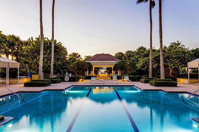 pool at dusk with a gazebo and a patio