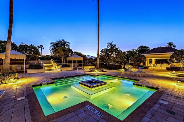 pool at dusk with a hot tub, a patio area, and a gazebo