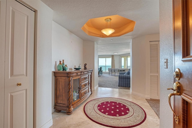 corridor with light carpet, a raised ceiling, and a textured ceiling