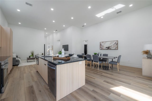 kitchen featuring light brown cabinets, light wood-type flooring, a kitchen island with sink, and stainless steel appliances