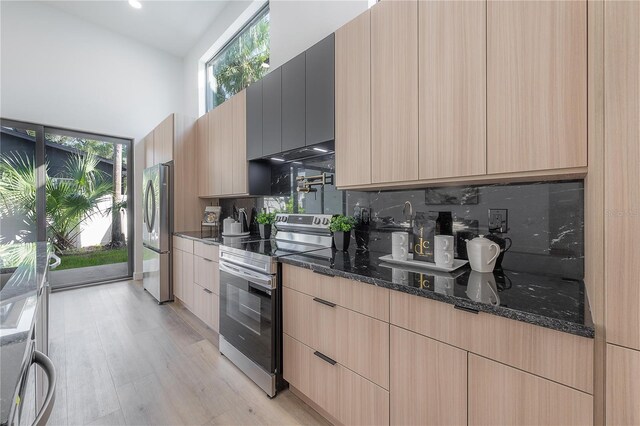 kitchen with light hardwood / wood-style flooring, backsplash, dark stone countertops, light brown cabinetry, and appliances with stainless steel finishes