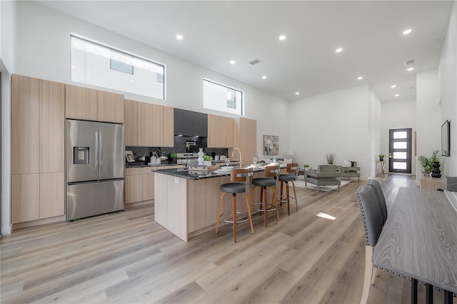 kitchen with an island with sink, light wood-type flooring, a high ceiling, and appliances with stainless steel finishes