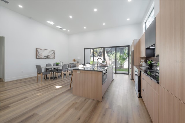 kitchen with a high ceiling, light hardwood / wood-style flooring, an island with sink, a breakfast bar area, and appliances with stainless steel finishes