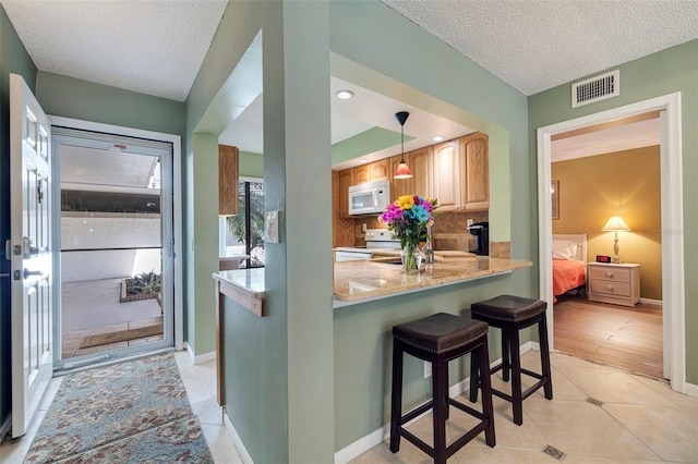 kitchen with light stone counters, white appliances, backsplash, hanging light fixtures, and a kitchen breakfast bar