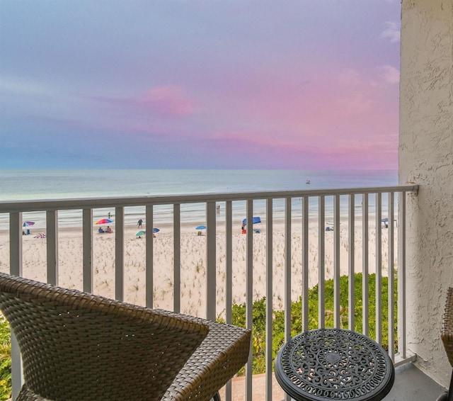 balcony at dusk featuring a water view and a view of the beach