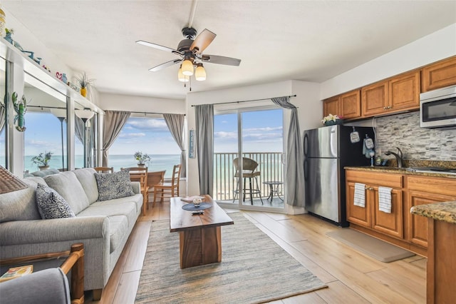 living room with ceiling fan, light hardwood / wood-style flooring, and a water view