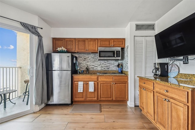 kitchen featuring appliances with stainless steel finishes, light wood-type flooring, dark stone counters, and backsplash