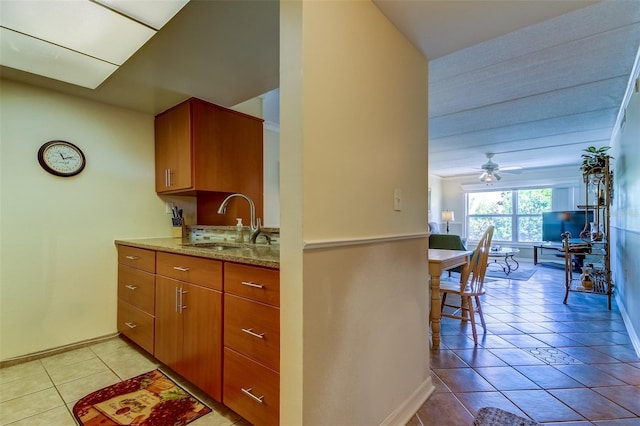 kitchen with light stone counters, sink, ceiling fan, and light tile floors