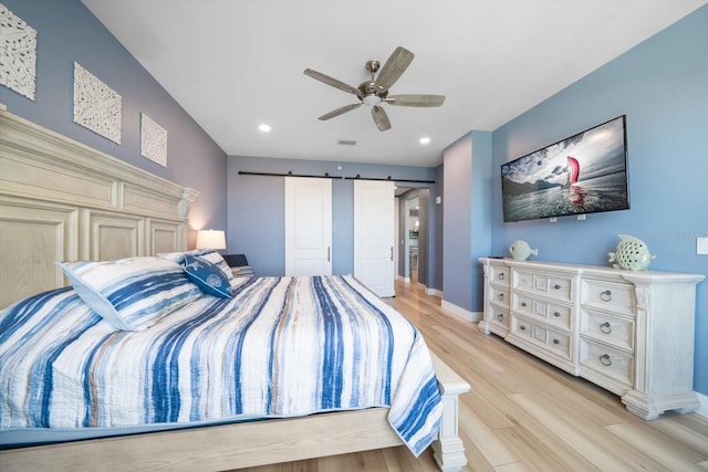 bedroom with light hardwood / wood-style flooring, a barn door, and ceiling fan