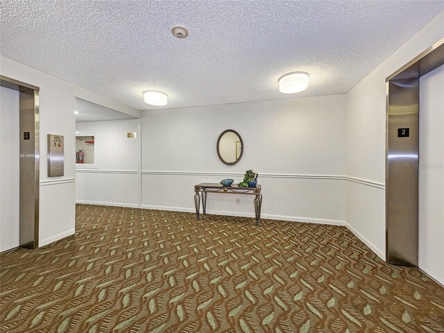 empty room with baseboards, dark colored carpet, a textured ceiling, and elevator