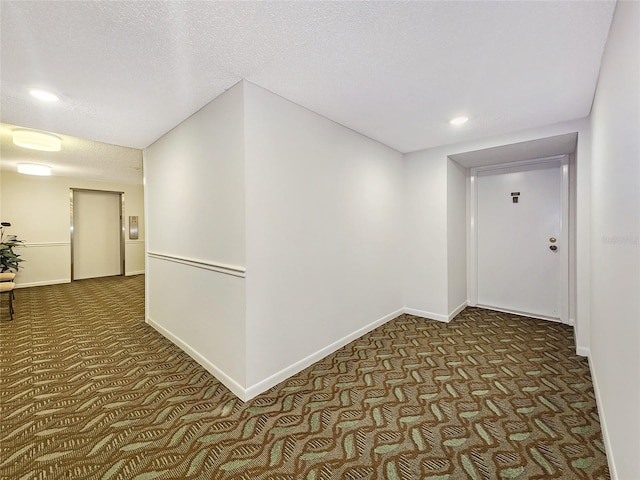 hallway featuring a textured ceiling and dark colored carpet