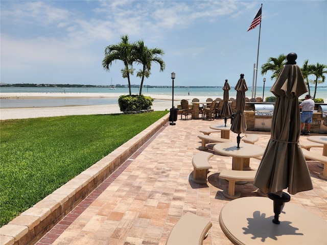 view of community featuring a view of the beach, exterior kitchen, a yard, a water view, and a patio