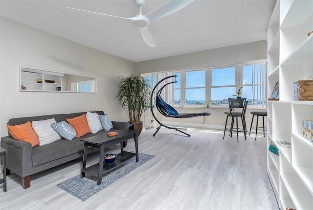 living room with light hardwood / wood-style floors, ceiling fan, and a textured ceiling