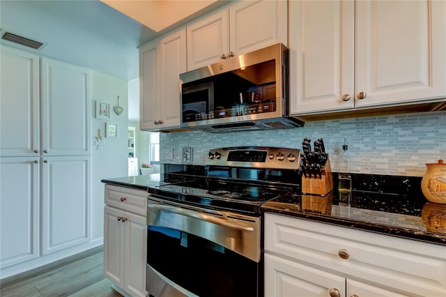 kitchen with white cabinets, stainless steel appliances, tasteful backsplash, dark stone countertops, and light hardwood / wood-style floors