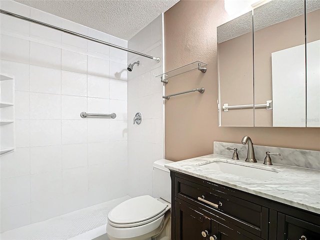 bathroom with a textured ceiling, vanity, toilet, and tiled shower