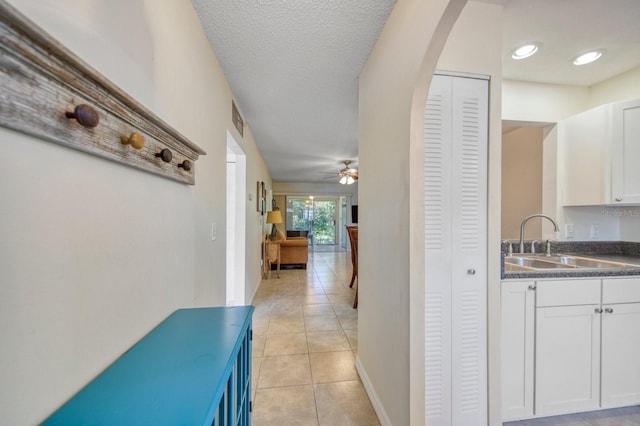 corridor featuring sink, light tile floors, and a textured ceiling