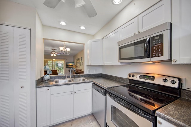 kitchen with appliances with stainless steel finishes, light tile floors, white cabinets, sink, and ceiling fan with notable chandelier