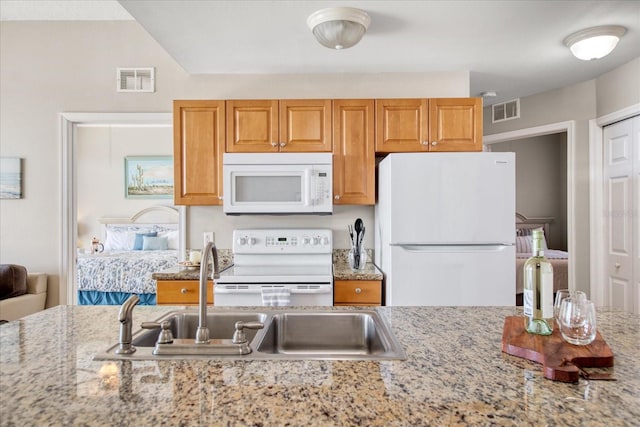 kitchen with white appliances, light stone counters, and sink