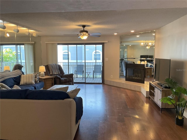 living room featuring ceiling fan, a textured ceiling, dark wood-type flooring, and a tiled fireplace