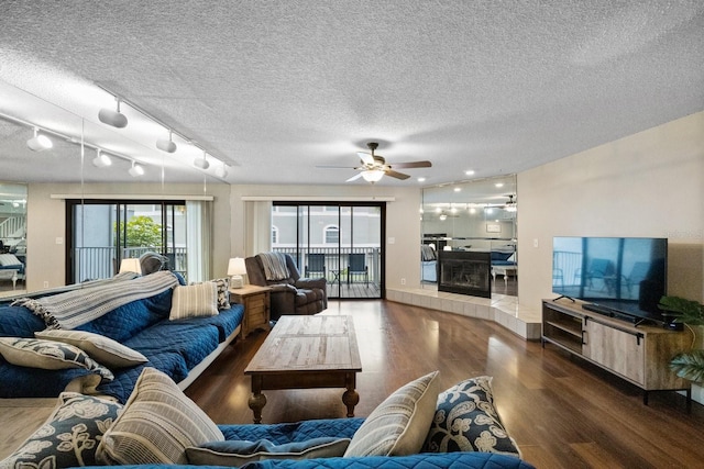 living room featuring a tiled fireplace, dark hardwood / wood-style floors, rail lighting, ceiling fan, and a textured ceiling