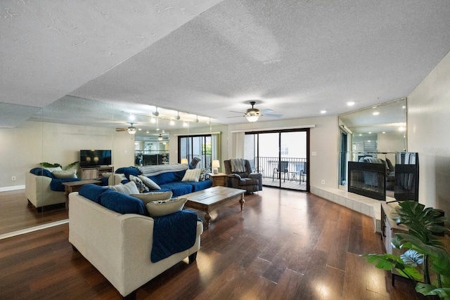 living room with ceiling fan, a textured ceiling, a tiled fireplace, dark hardwood / wood-style flooring, and track lighting