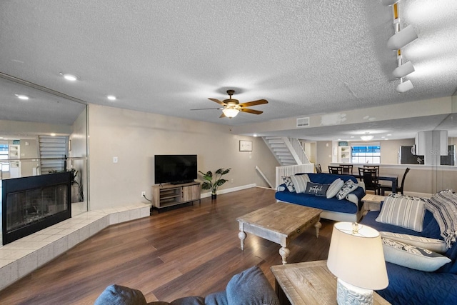 living room with ceiling fan, a textured ceiling, dark wood-type flooring, and a tile fireplace