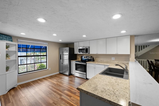 kitchen featuring white cabinets, light stone countertops, dark wood-type flooring, appliances with stainless steel finishes, and sink