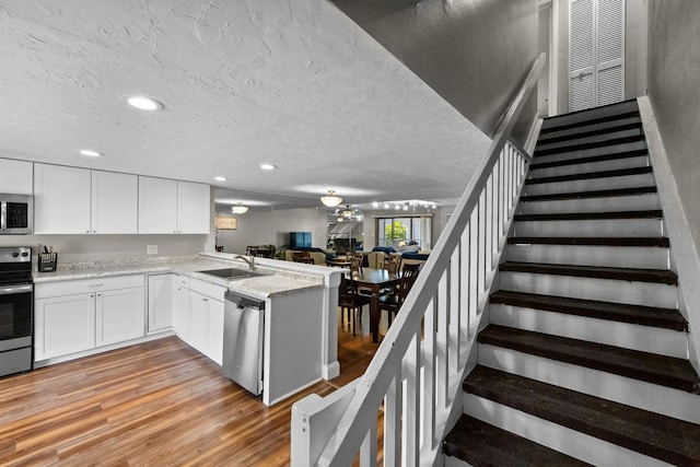 kitchen featuring white cabinets, stainless steel appliances, sink, light hardwood / wood-style floors, and a textured ceiling