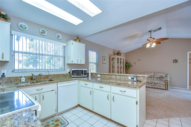 kitchen featuring ceiling fan, white cabinetry, vaulted ceiling with skylight, kitchen peninsula, and white dishwasher