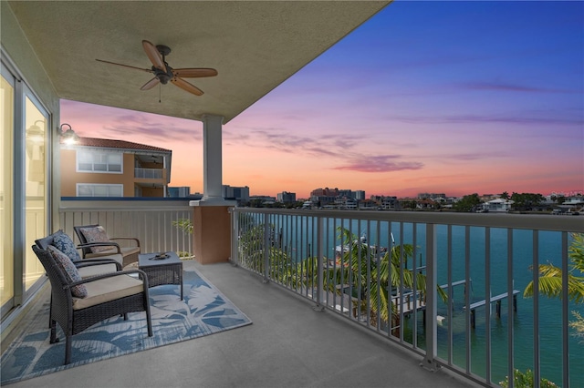 balcony at dusk with a water view and ceiling fan