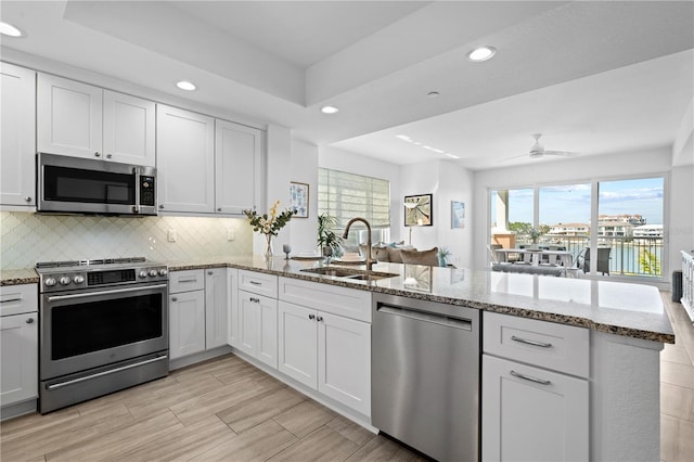 kitchen featuring ceiling fan, sink, backsplash, stainless steel appliances, and kitchen peninsula